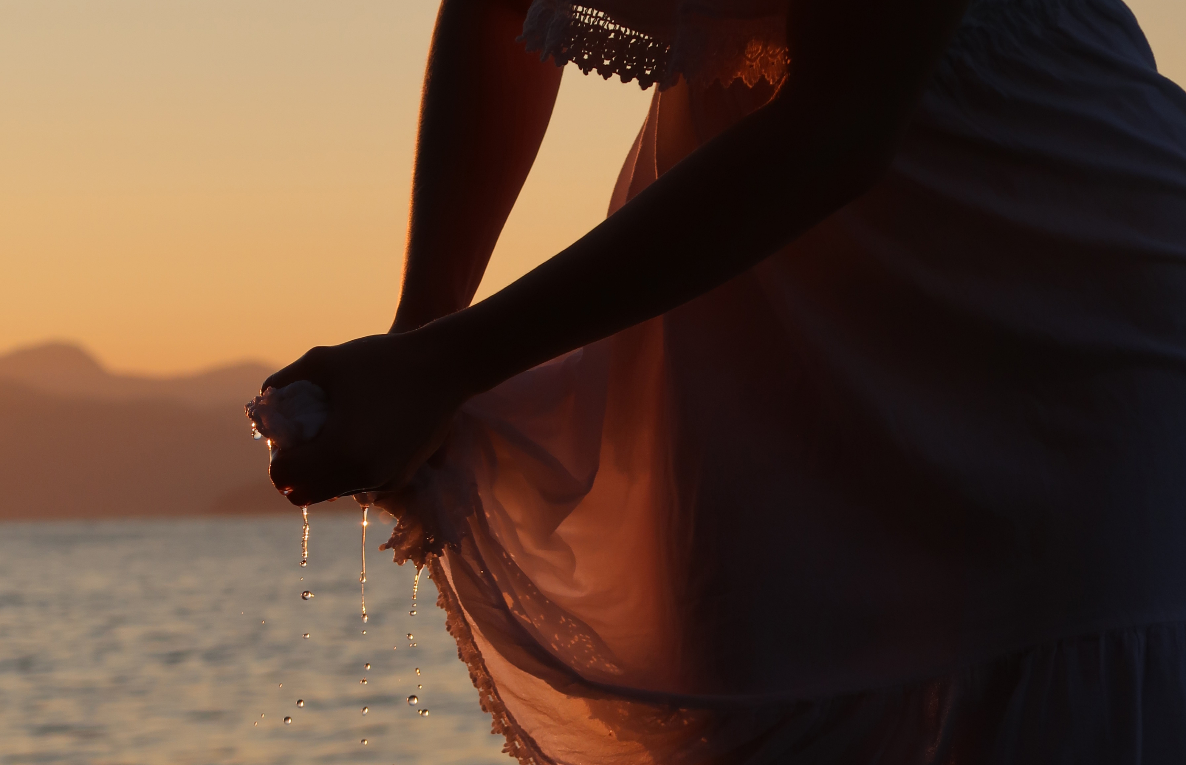 Two girls in white shirts are looking away while tangled in ropes with flowers in a grass field during sunset